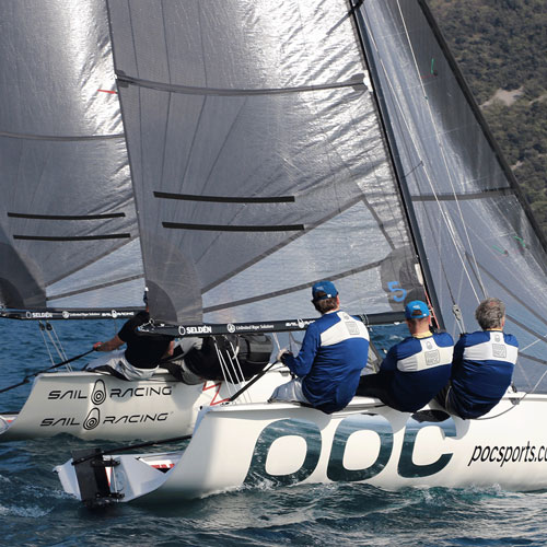 Sailors leaning over the side of a racing sailboat, with another boat close alongside.
